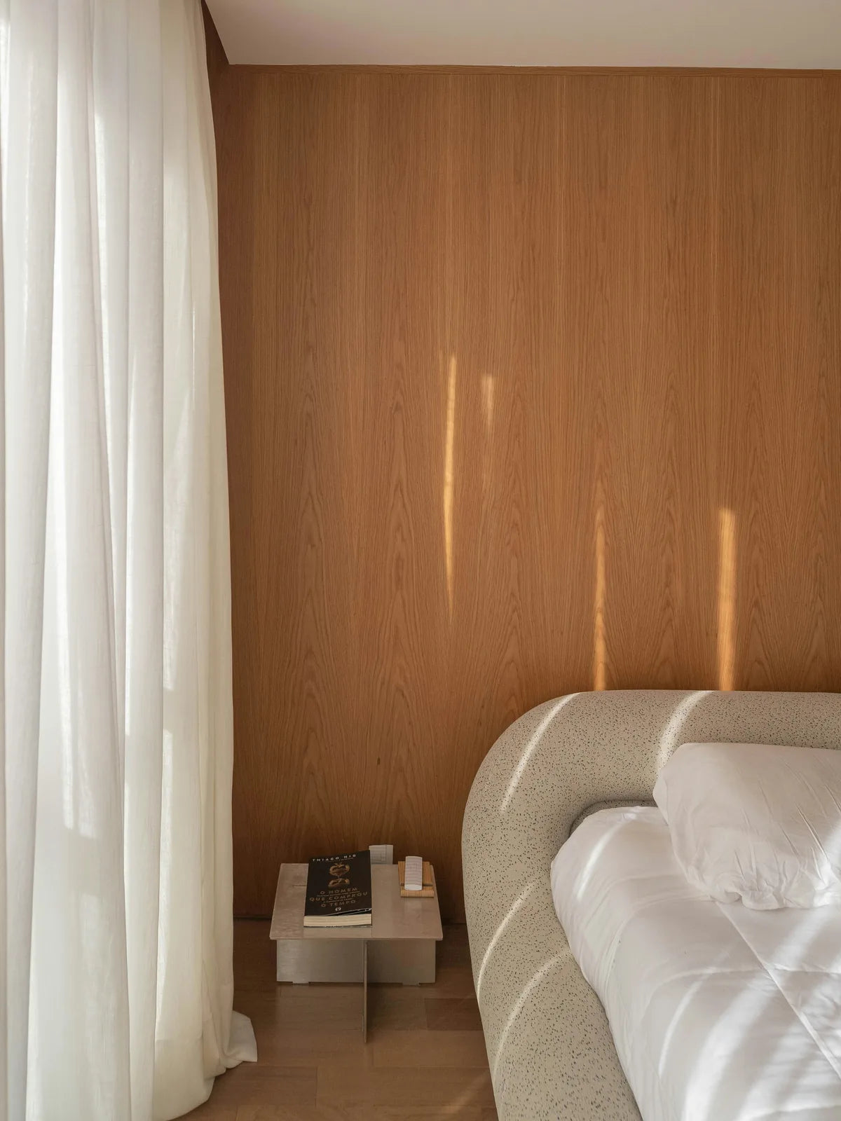 A bedroom corner: wood panelling, a linen curtain, and a bed against the wall.