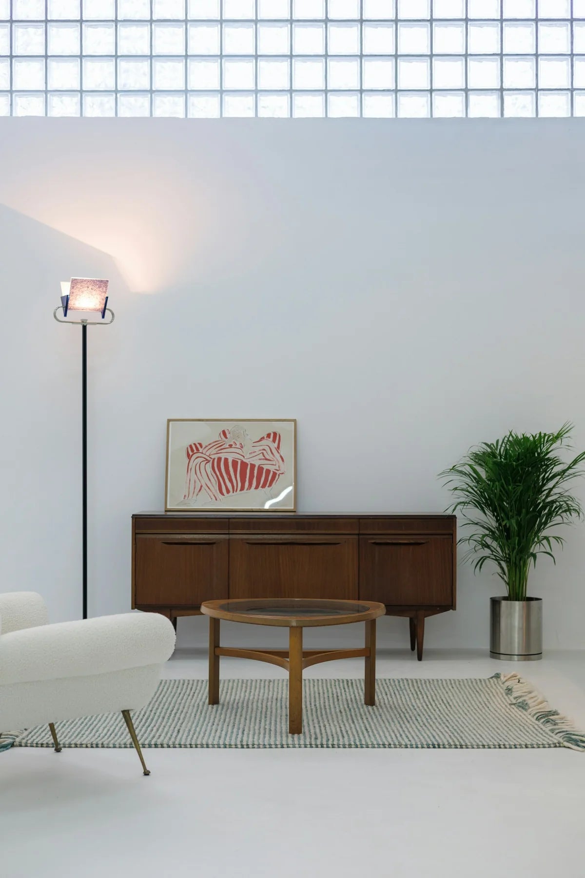 A pale modernist living room with sculptural white seating, a walnut cabinet and glass block.